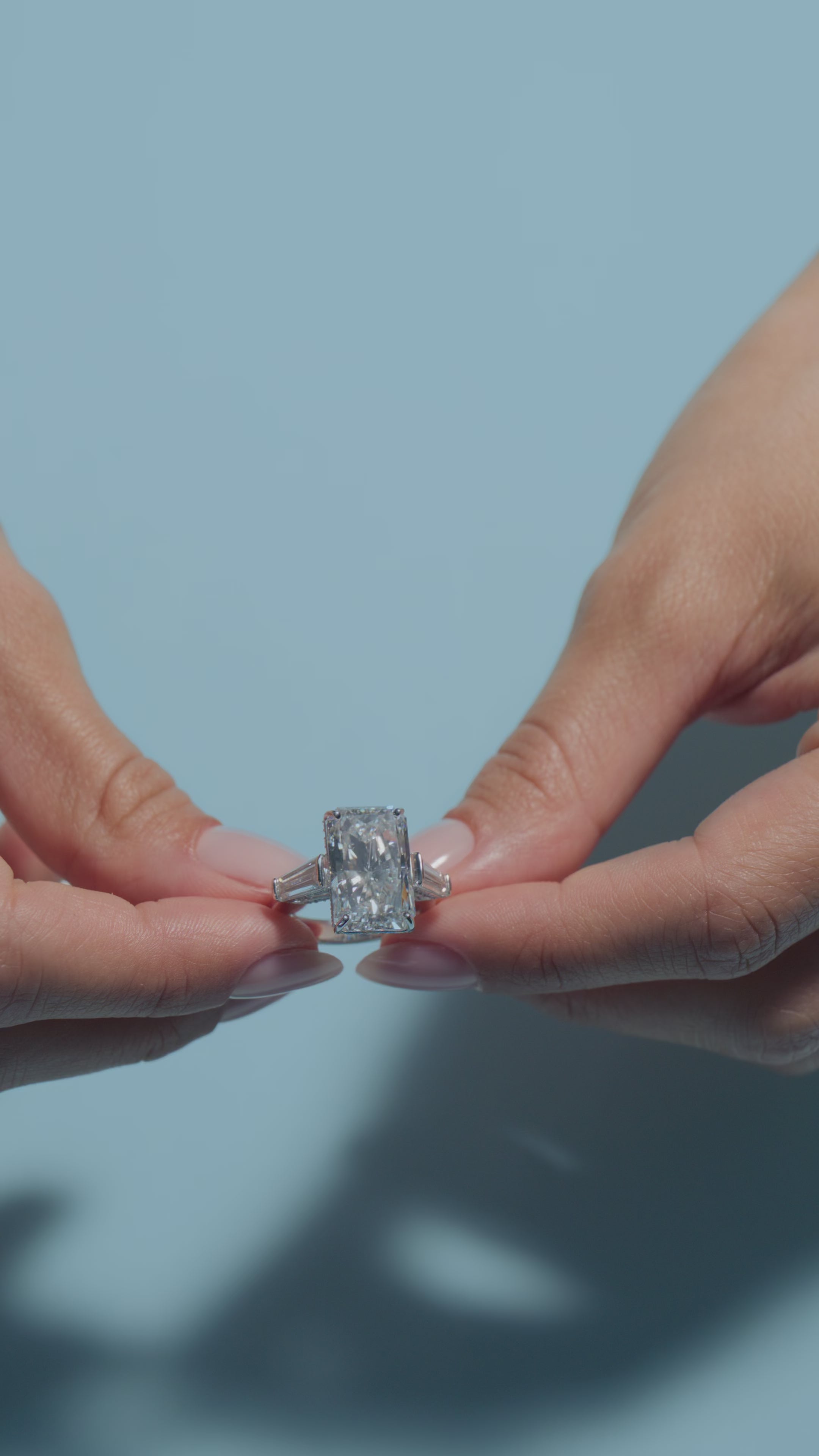 A video of an 8.59ct Radiant Lab Diamond Intricate Trilogy Ring shown by the model on a light blue background