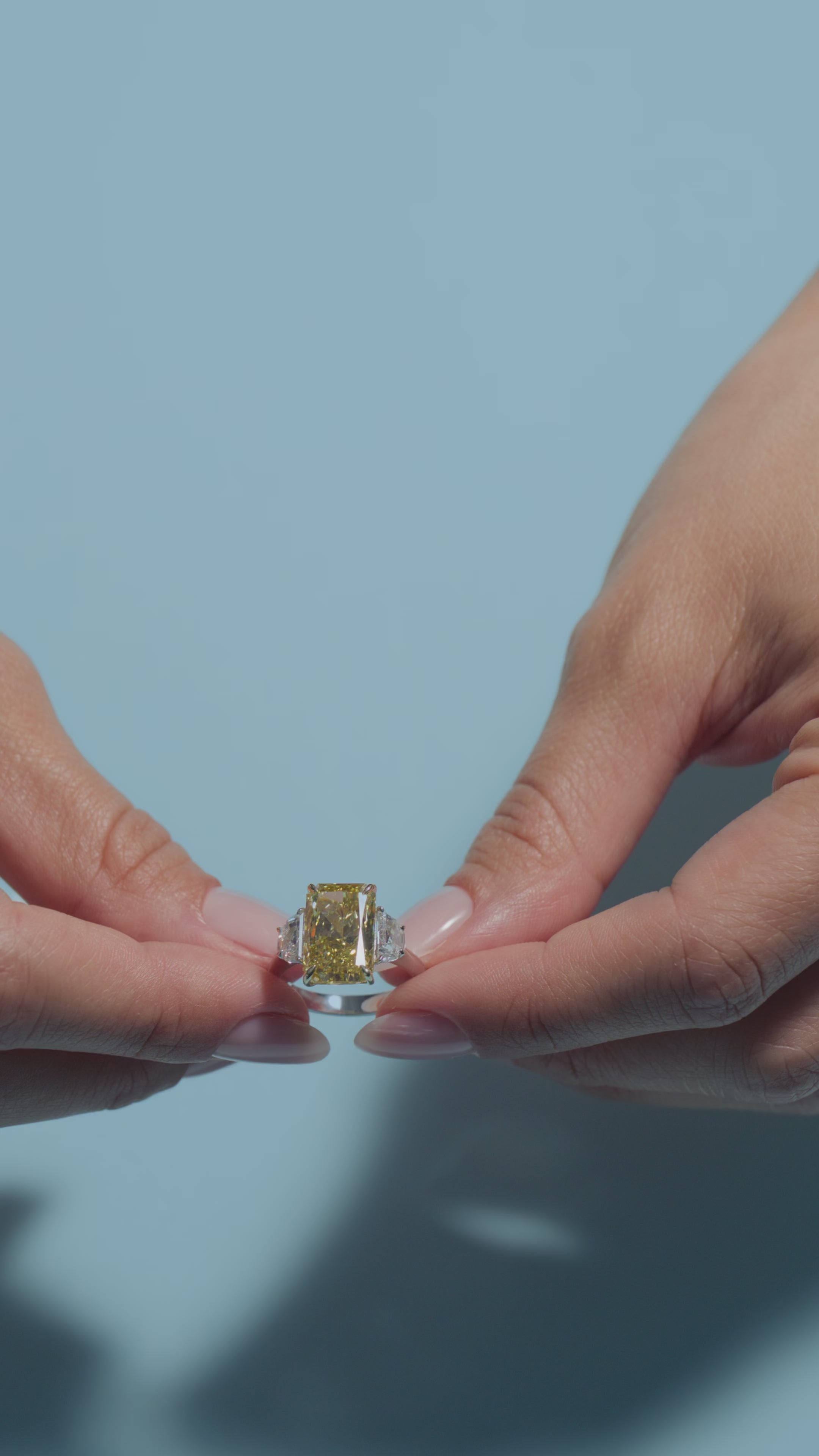 A video of a 5.01ct Fancy Intense Yellow Radiant Lab Diamond Classic Trilogy Ring presented by the model of BAL Diamonds on a light blue background