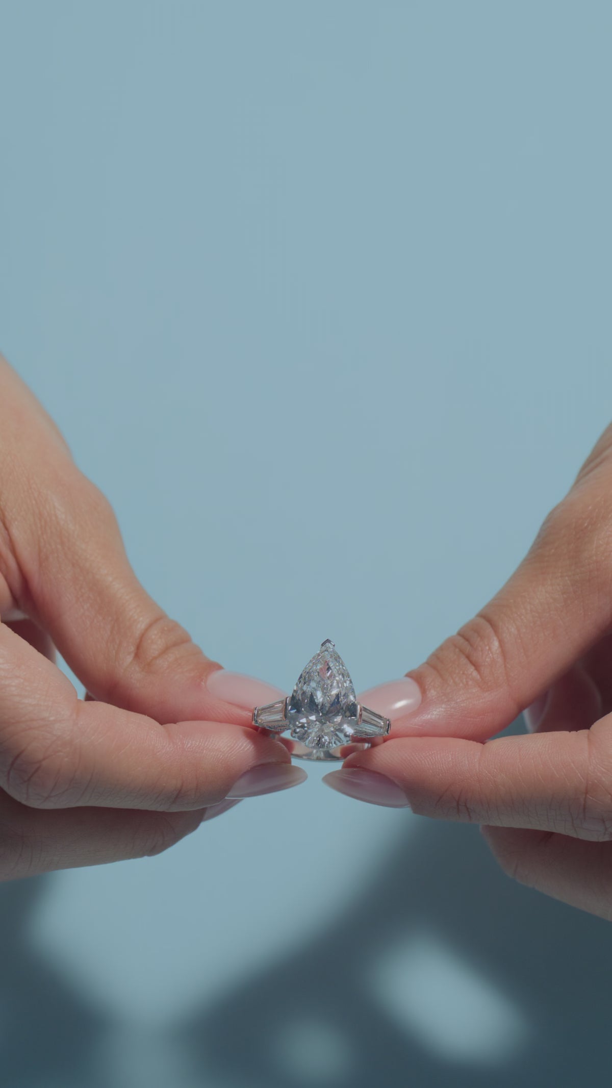 A video clip of a 7.1ct Pear Lab Diamond Intricate Trilogy Ring held and worn by the model of BAL Diamonds on a light blue background 