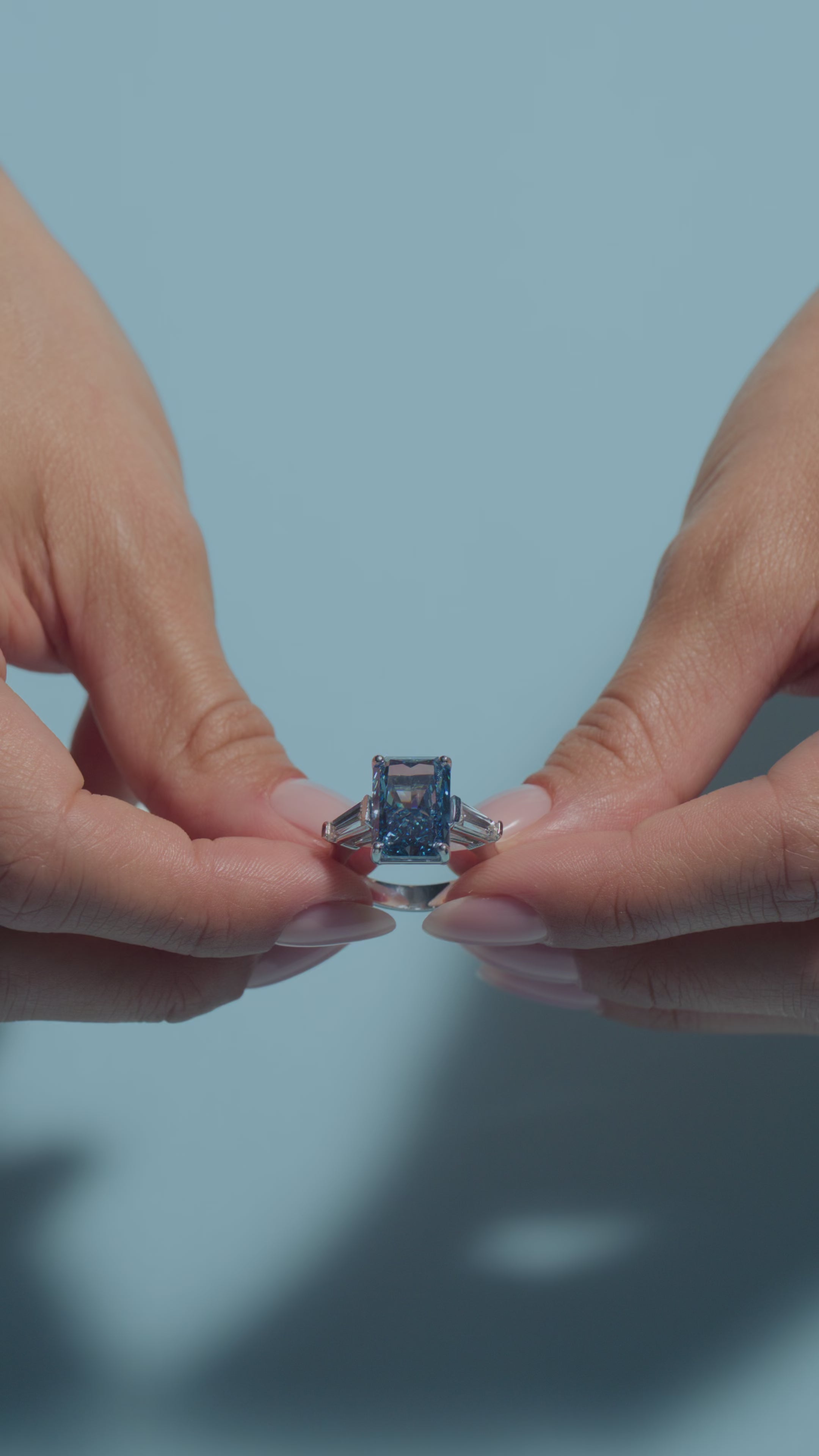 A video clip of a 6.66ct Radiant Fancy Vivid Blue Lab Diamond Tapers Trilogy Ring shown off by the model of BAL Diamonds on a light blue background 