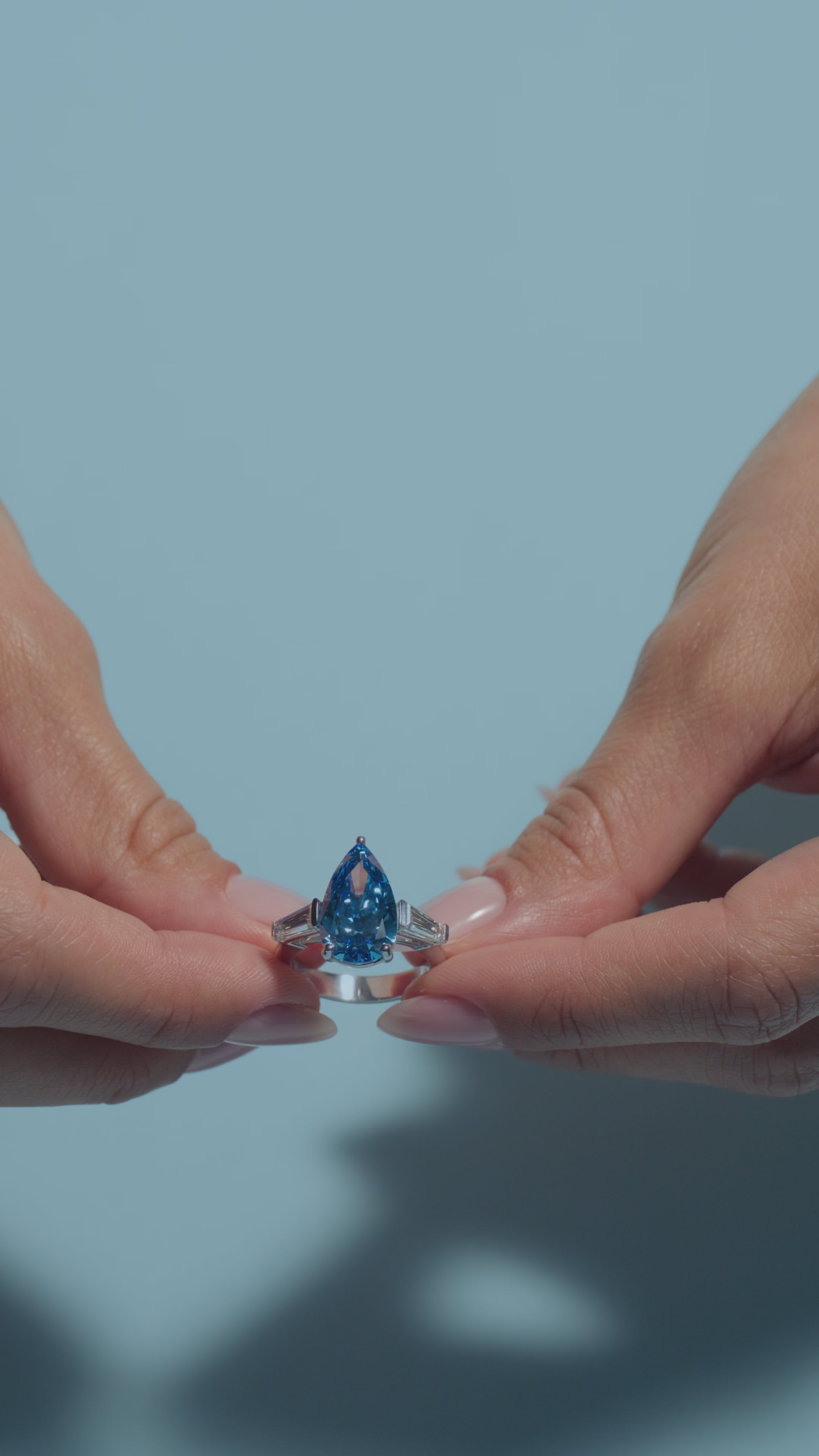 A short video featuring a 5ct Pear Fancy Vivid Blue Lab Diamond Tapers Trilogy Ring held by the  model on a light blue background 