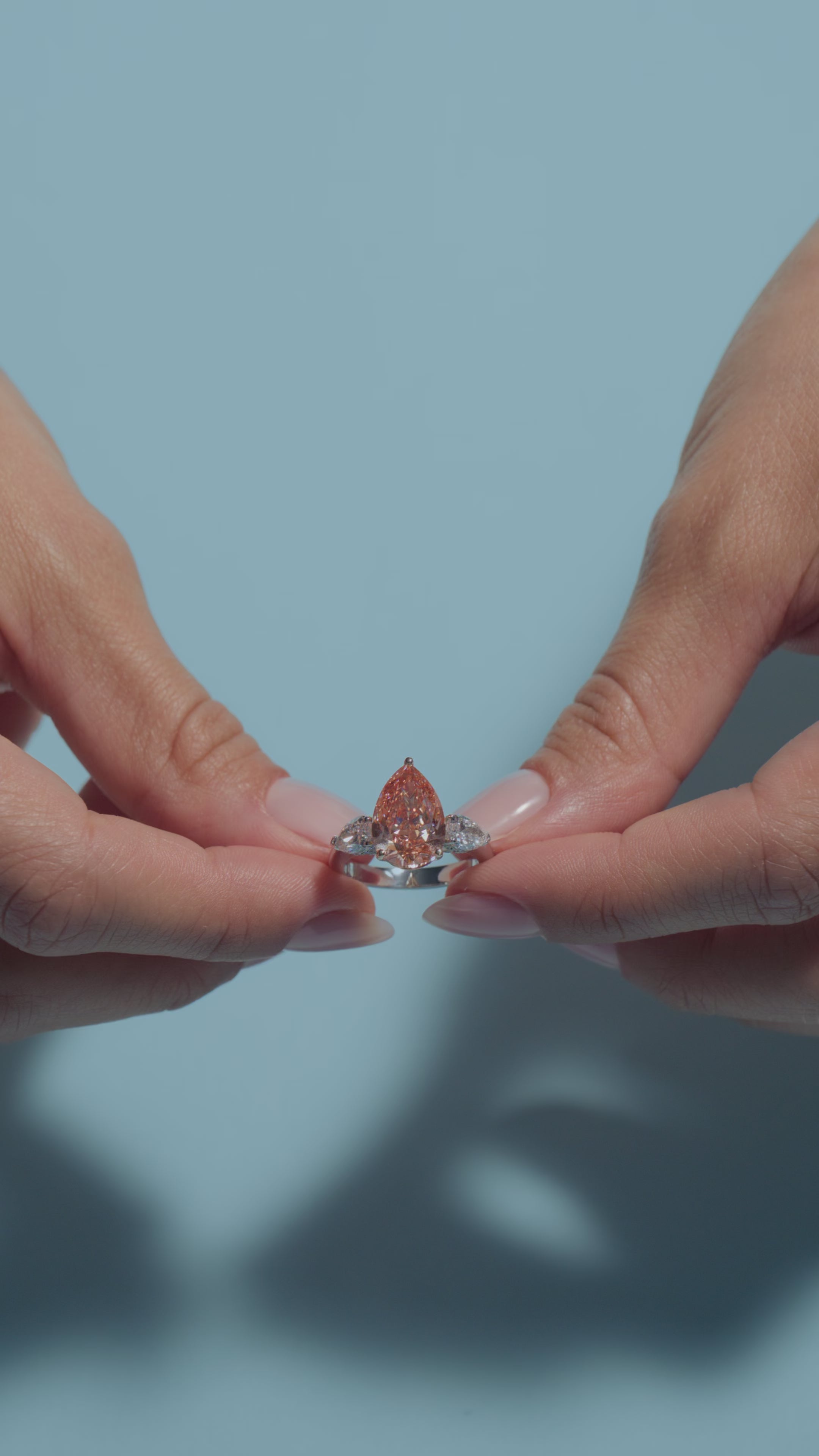 A short video of a 4.54ct Pear Fancy Vivid Orangy Pink Lab Diamond Pear Trilogy Ring presented by the model of BAL Diamonds on a light blue background 