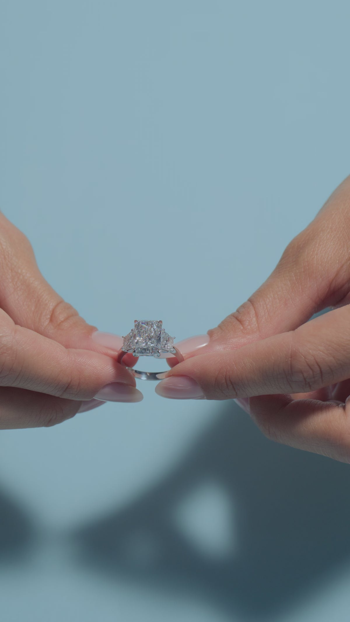 A video presenting a 4.06ct Radiant Lab Diamond Classic Trilogy Ring held and worn by the model on a light blue background